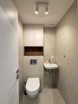 Small bathroom with a toilet, washbasin, and built-in storage units. - image 16