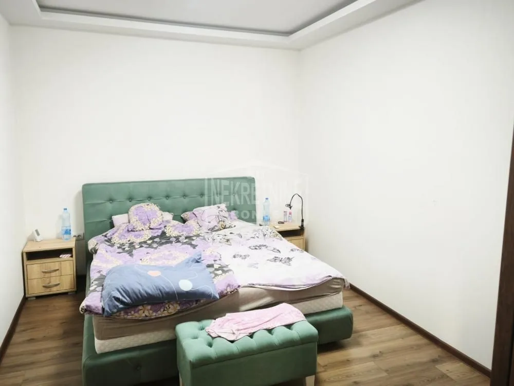 Spavaća soba sa bračnim krevetom sa zelenim tapaciranim uzglavljem i noćnim stočićima.