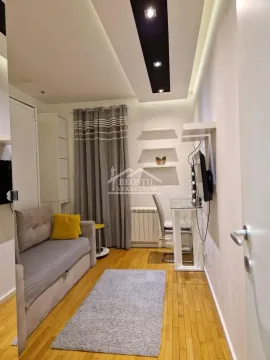 Small living room with a sofa, desk, and dropped ceiling with lighting. - image 12