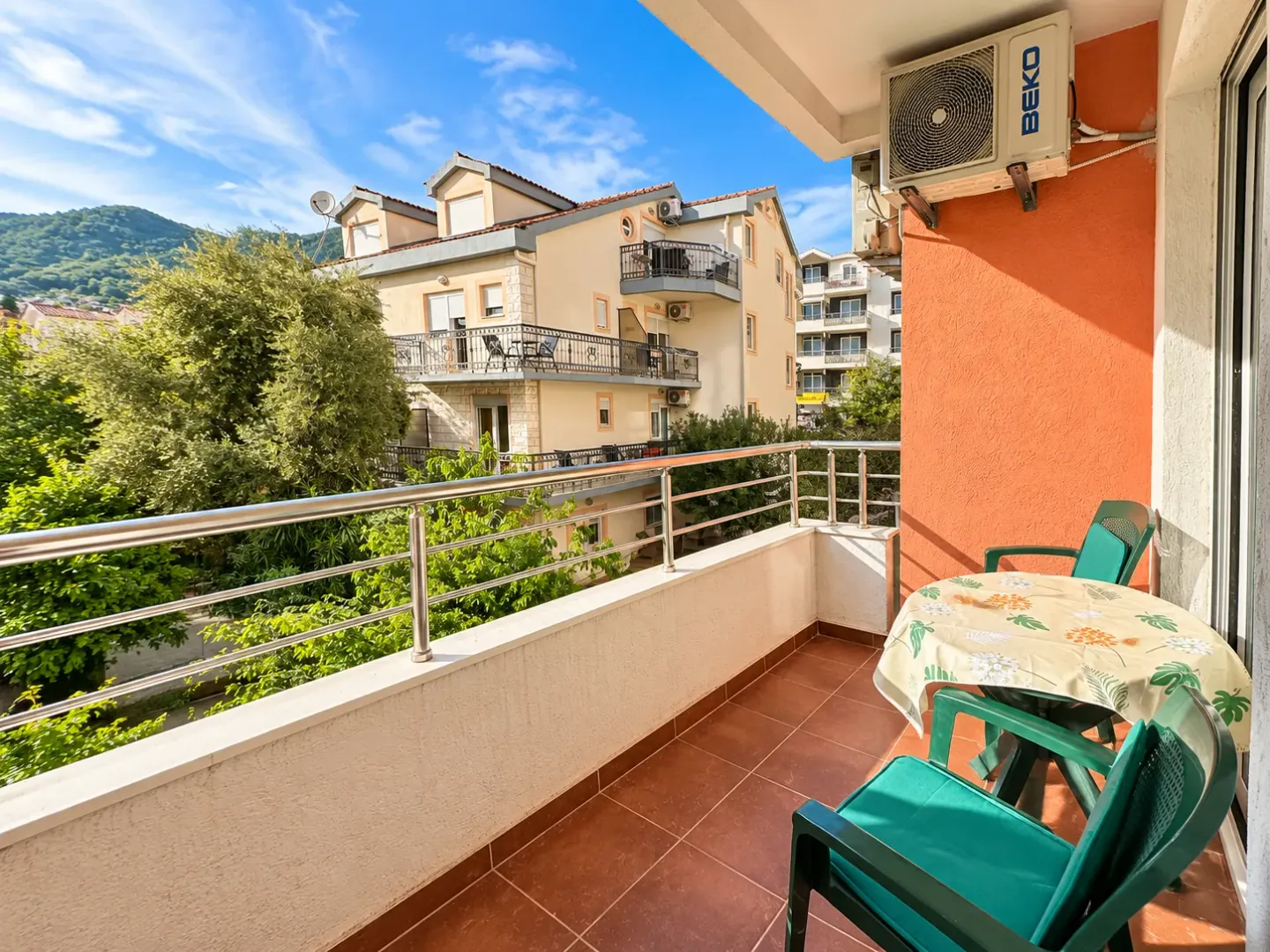 Furnished balcony with a table, chairs, and a view of neighboring buildings and greenery.
