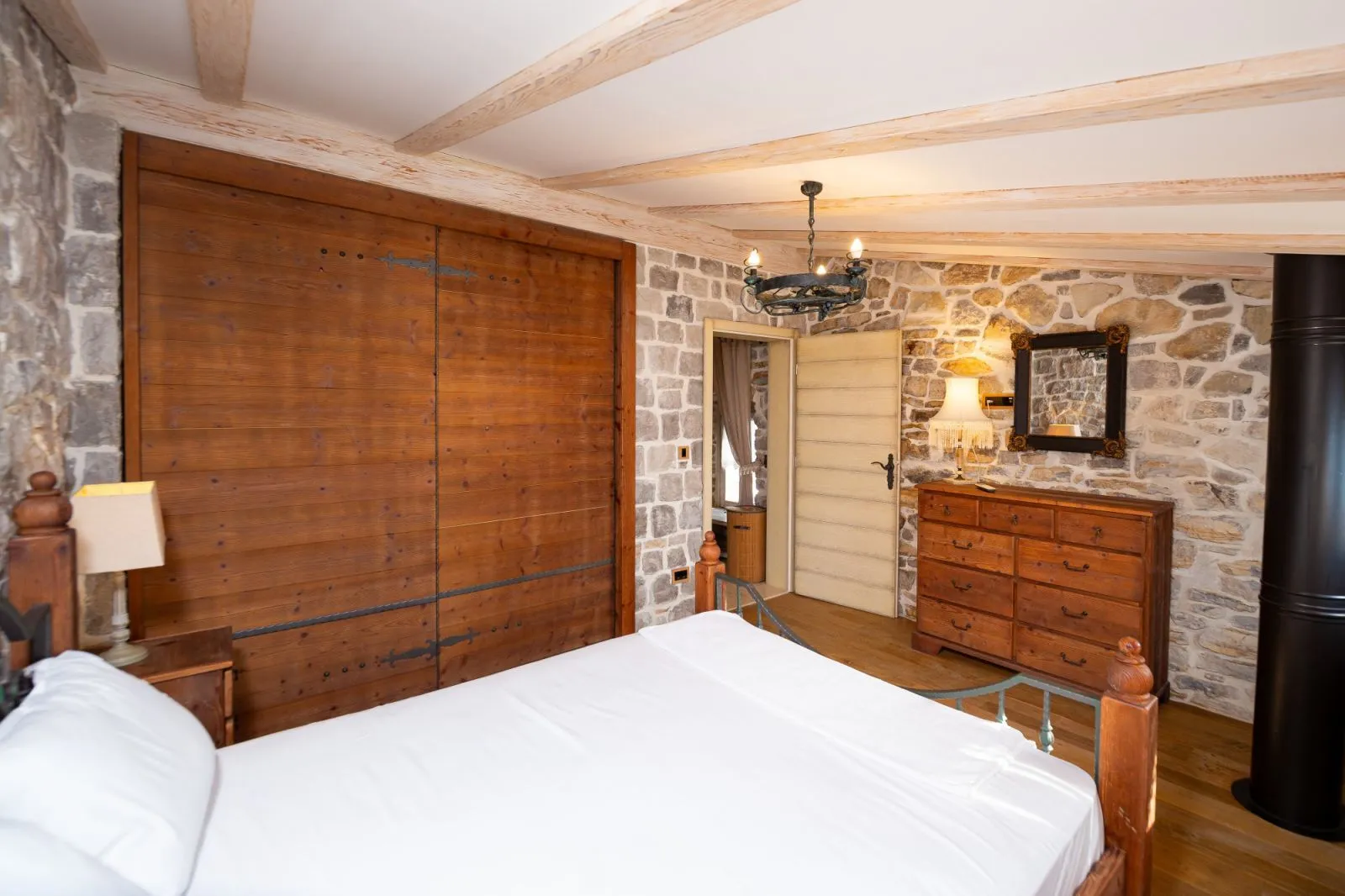 Rustic bedroom featuring stone walls, wooden ceiling beams, and solid wooden furniture.