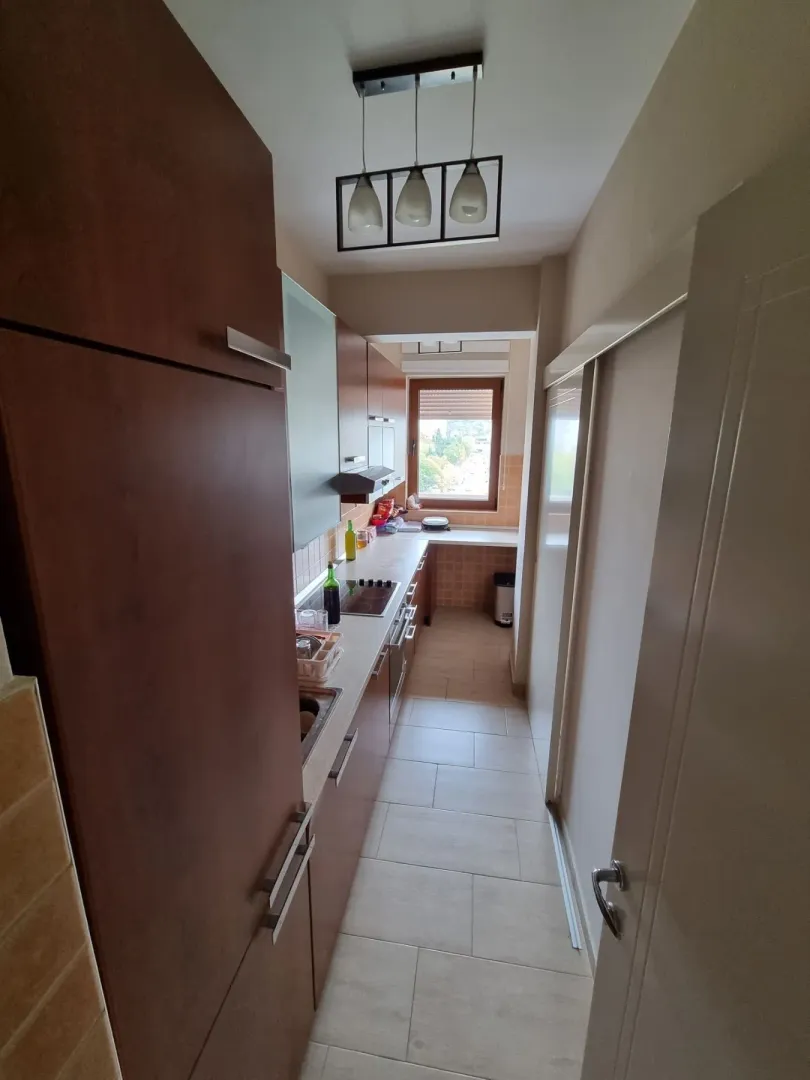 A narrow layout of a functional kitchen with brown cabinets and a window.