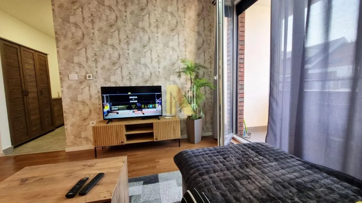 Dnevna soba sa TV-om, nameštajem i izlazom na terasu.