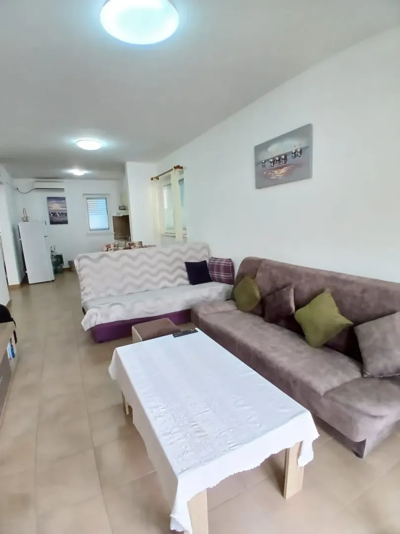 Dnevni boravak sa garniturom za sedenje, stočićem i pogledom na kuhinjski deo u pozadini.