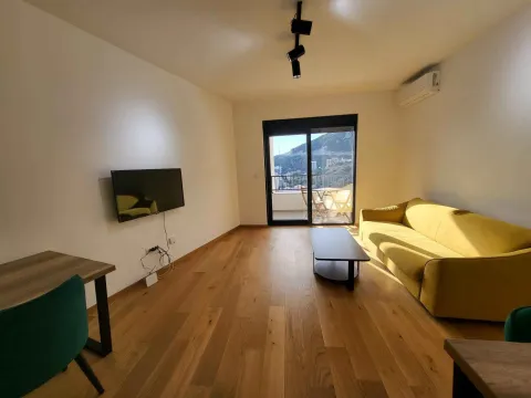 Dnevna soba sa žutim kaučem, TV-om na zidu i izlazom na terasu. - image 3