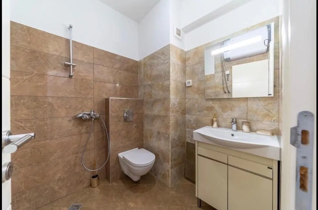 Bathroom tiled with ceramic tiles featuring a walk-in shower, washbasin, and toilet.