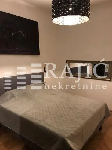 Spavaća soba sa bračnim krevetom, umetničkom slikom i lusterom.