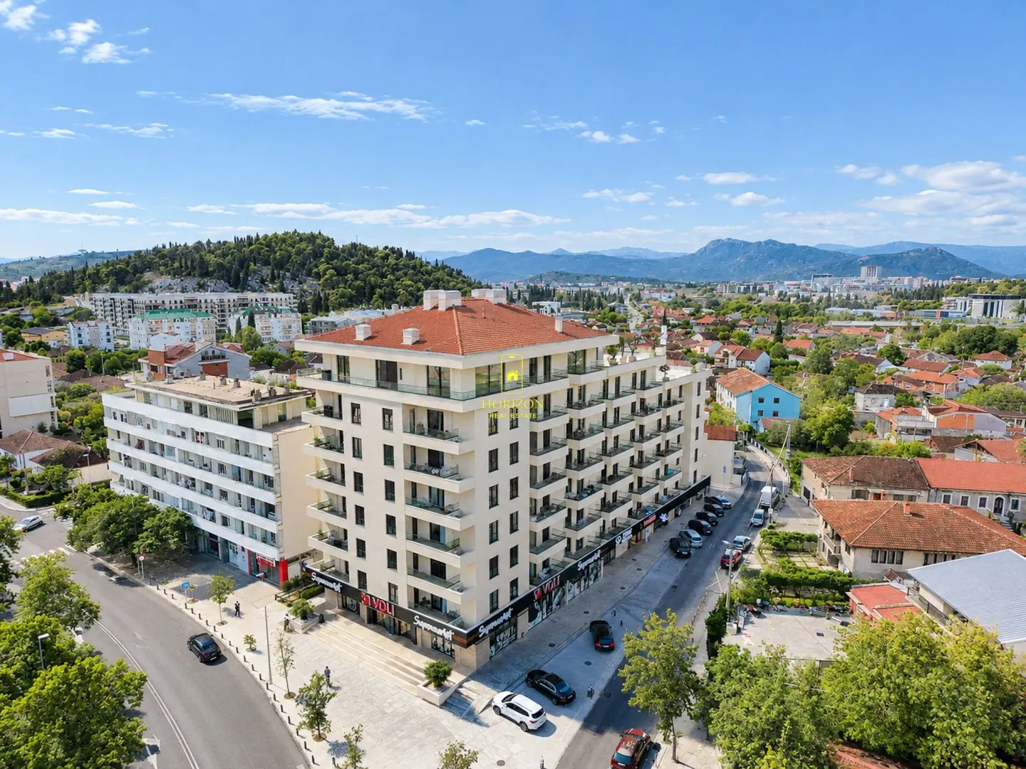Pogled iz vazduha na stambenu zgradu i okolno naselje.