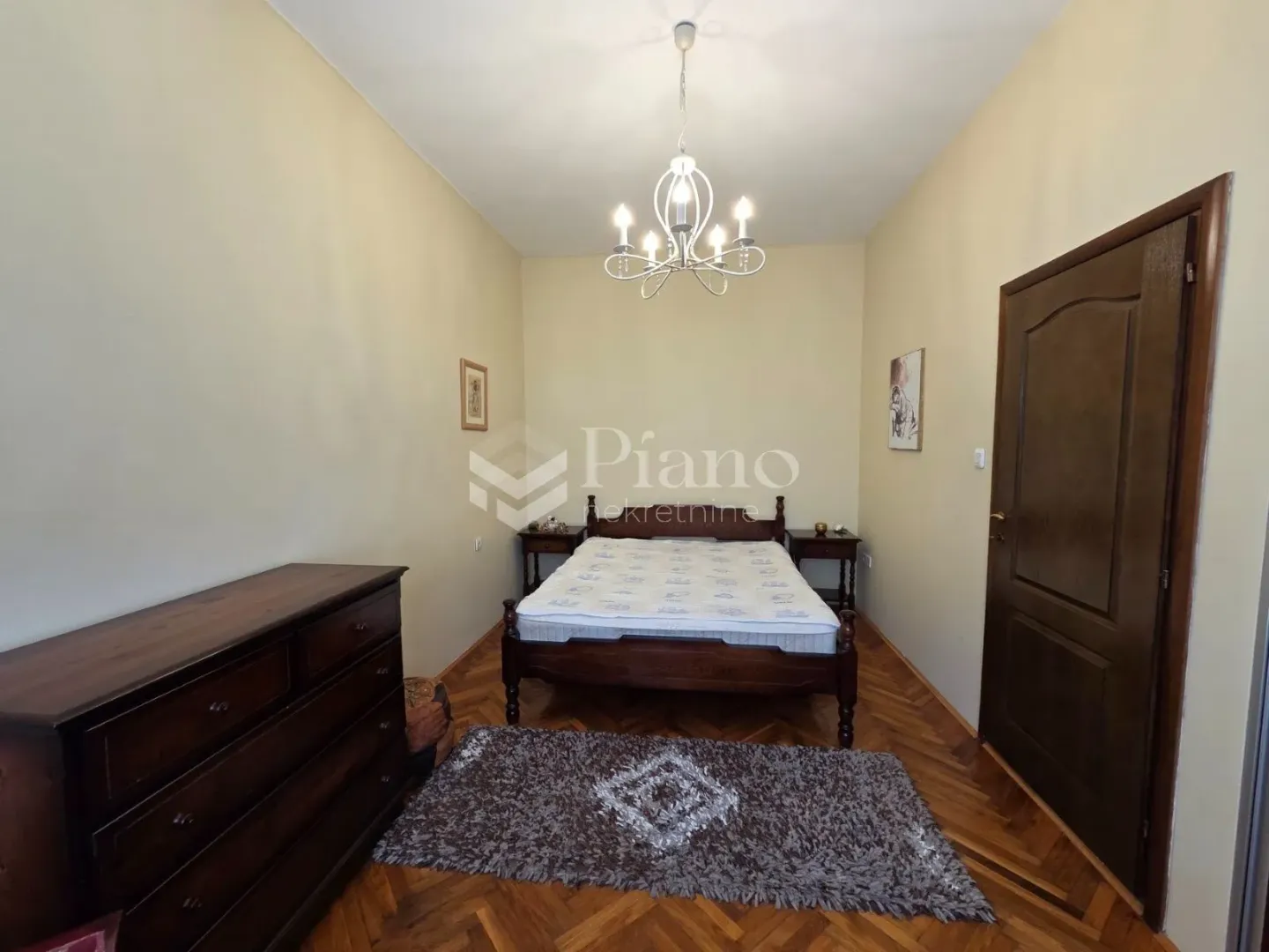 Bedroom with a double bed, wooden dresser, and parquet flooring.