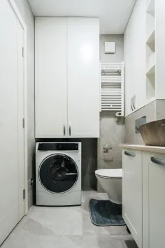 Modern bathroom with white cabinetry, washing machine, and toilet. - image 9