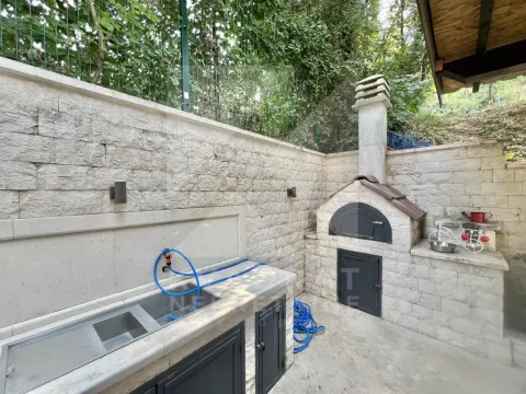 Yard with a built-in barbecue and sink next to a stone-clad wall. - image 12