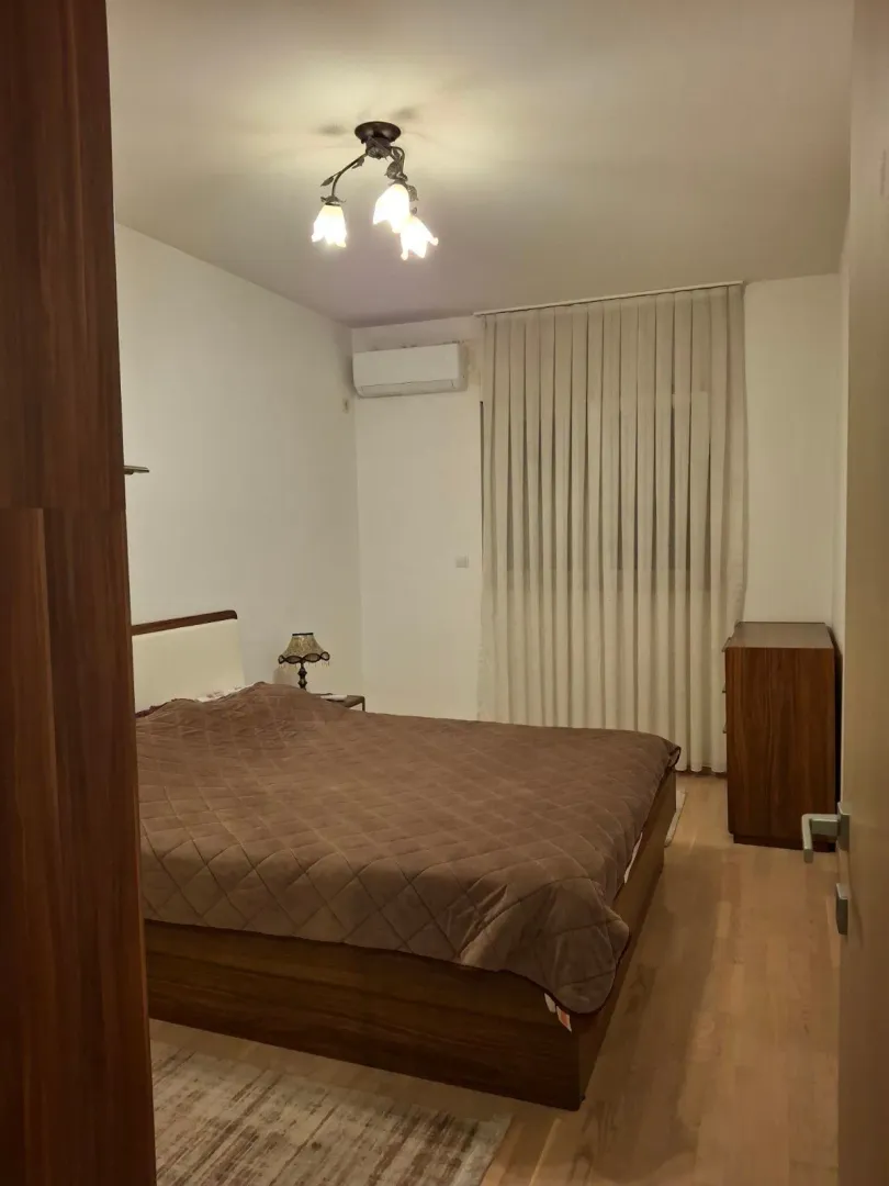Bedroom with a double bed, wooden dresser, and a window with curtains.
