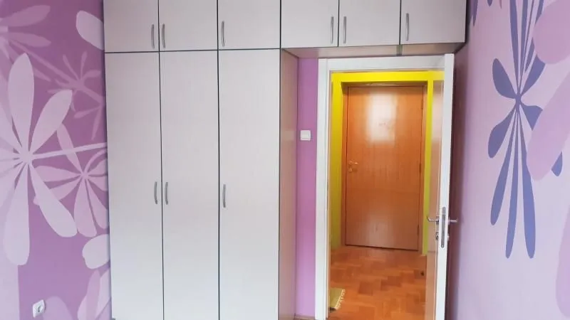 Spavaća soba sa velikim ugradnim garderoberom i ljubičastim tapetama sa cvetnim motivima.
