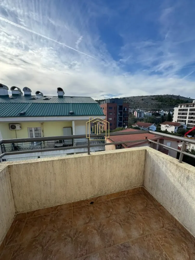 Manji popločani balkon sa metalnom ogradom i pogledom na okolne zgrade i brdo.