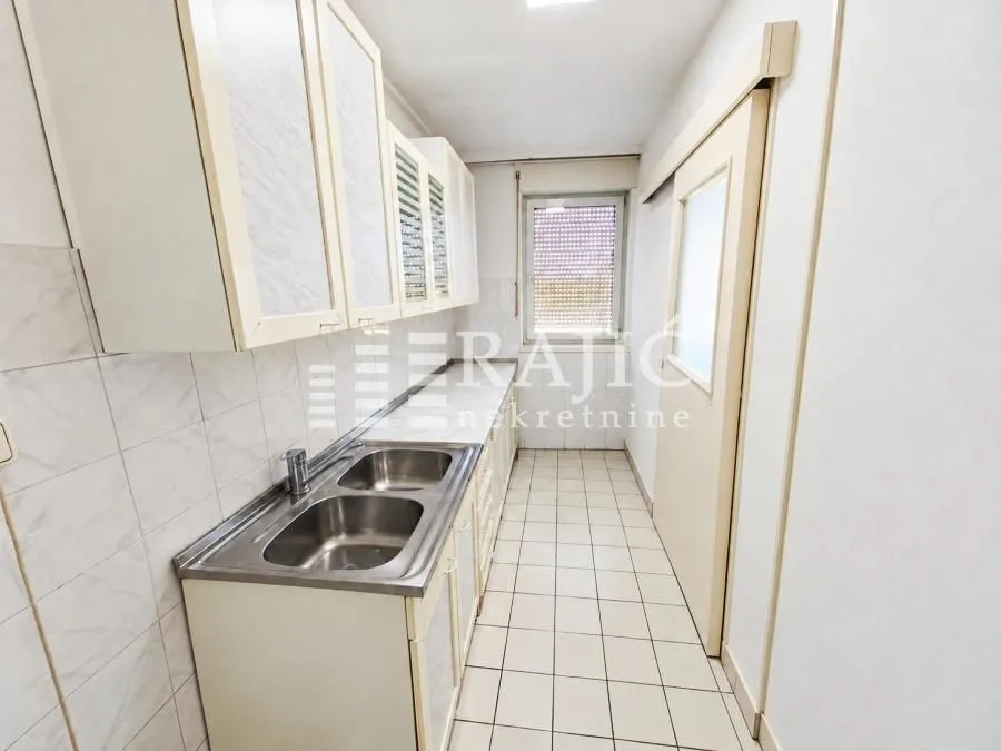 Small narrow kitchen with white cabinets and tiled floor.