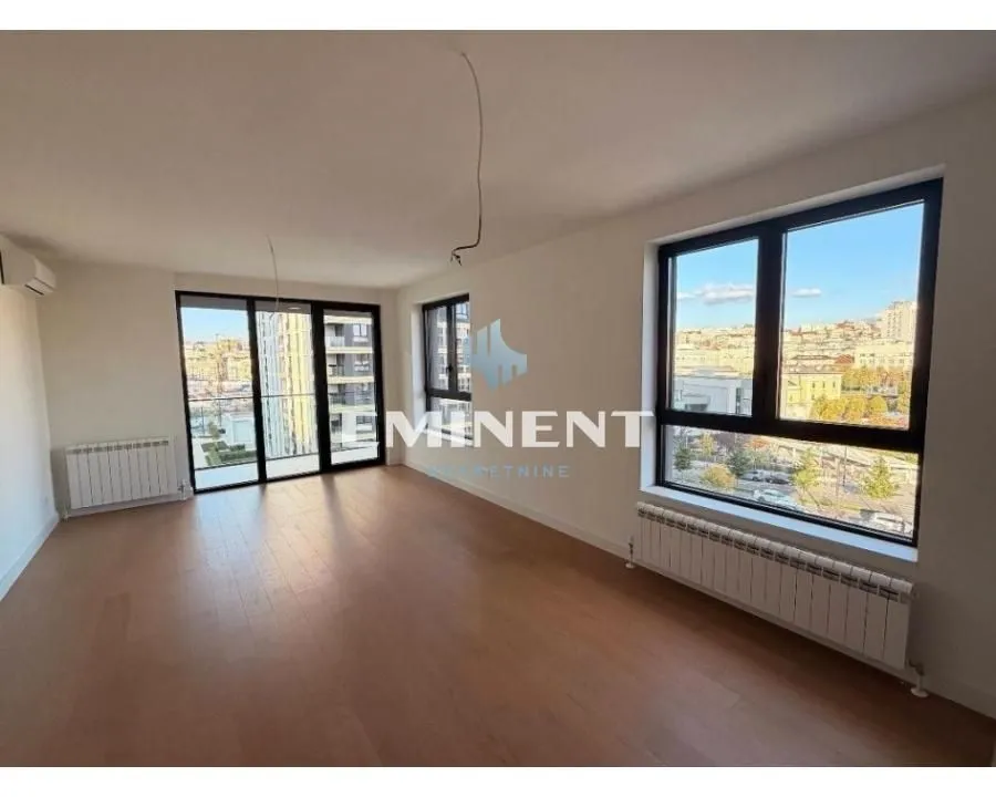 Empty bright room with wooden flooring, large windows, and a city view.