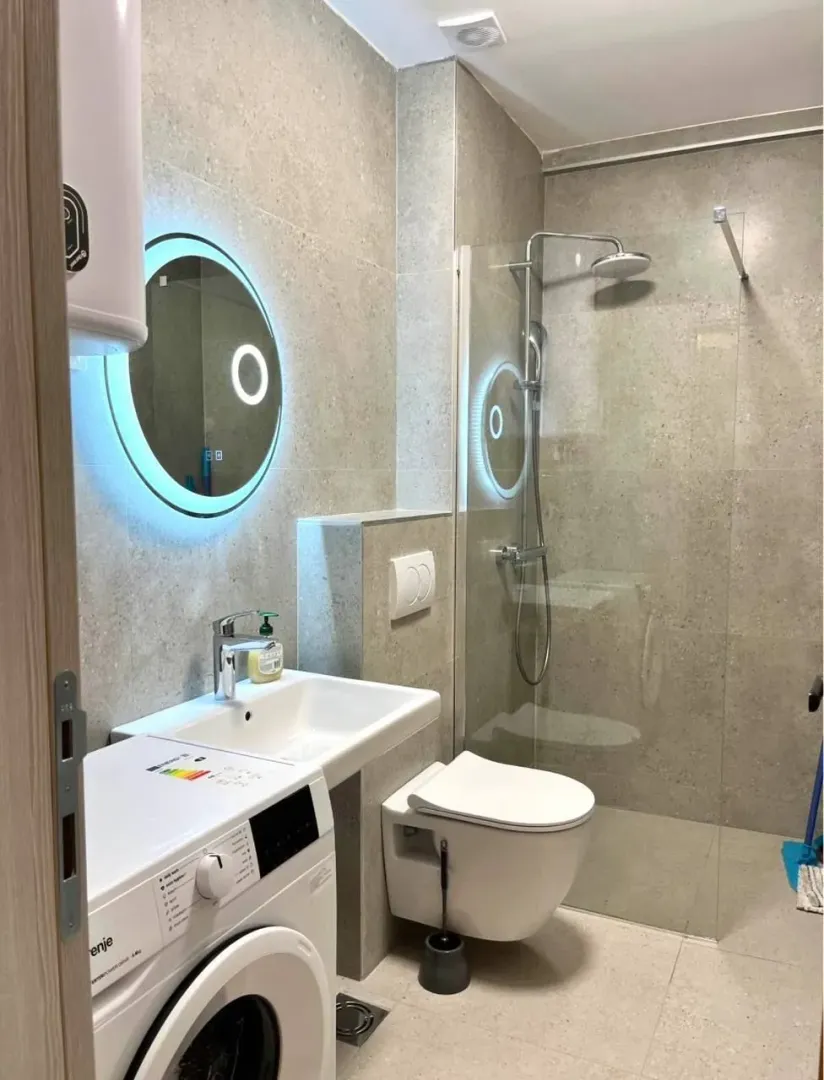 Modernly equipped bathroom with a walk-in shower, washbasin, and washing machine.