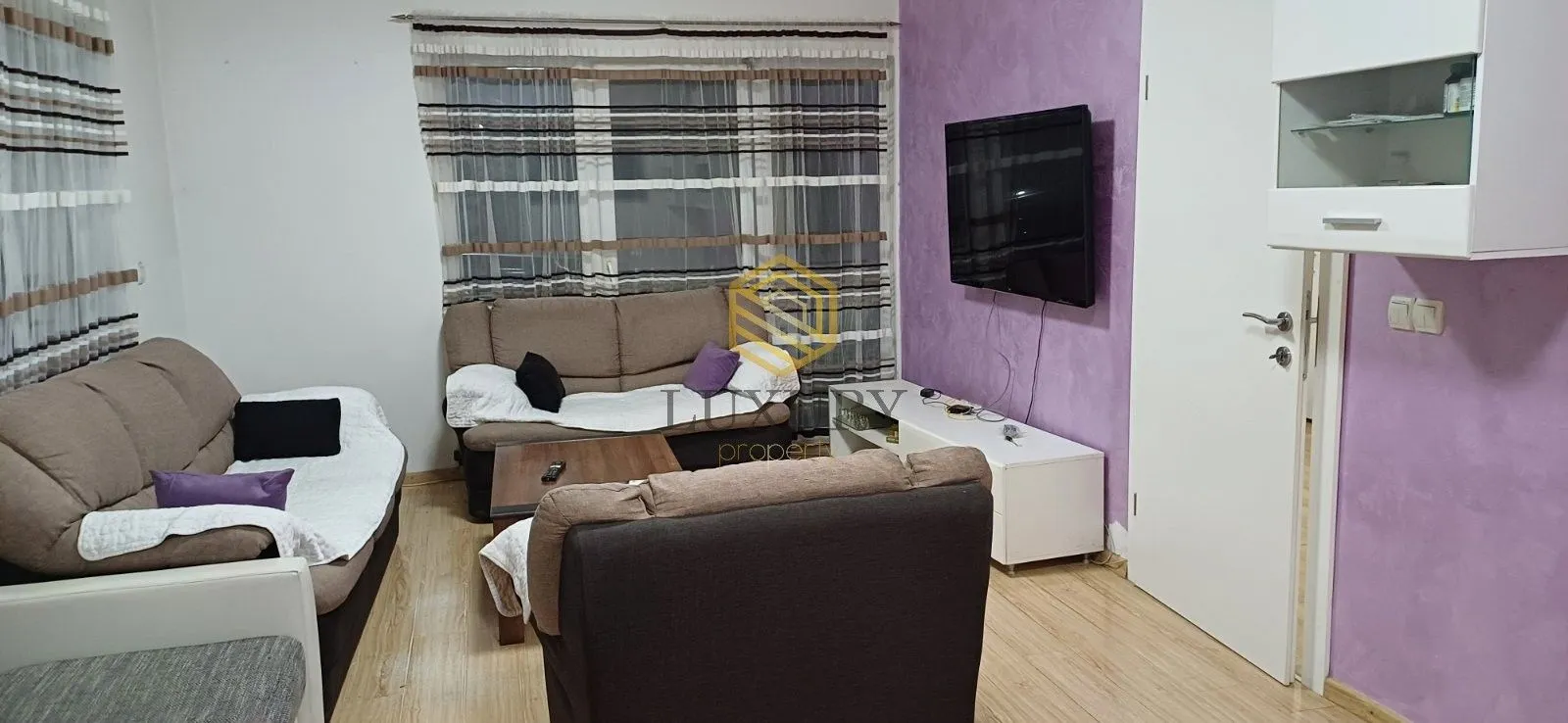 Living room with sofa set, TV and a purple wall.