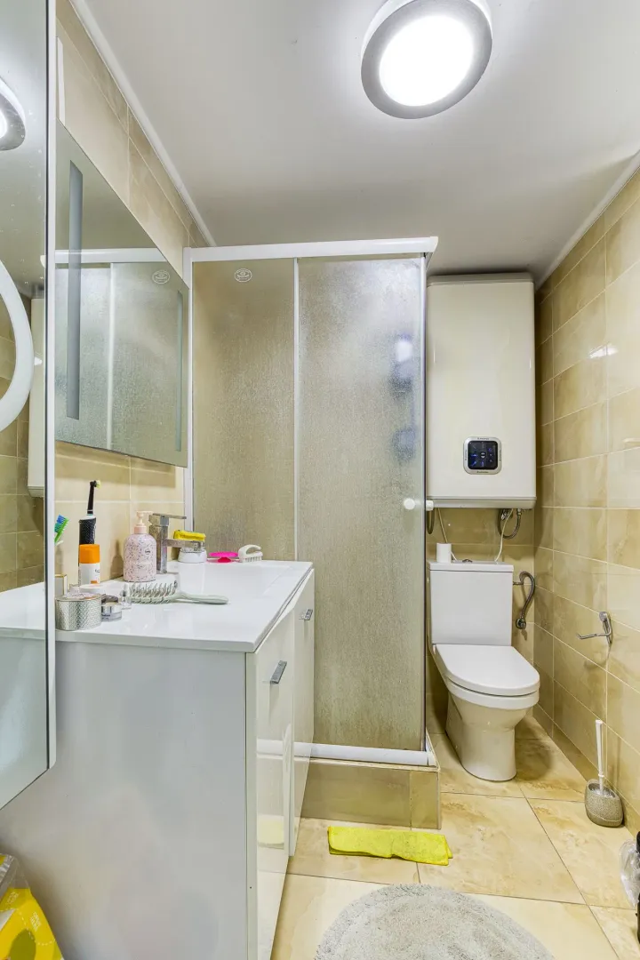 Manje kupatilo sa tuš kabinom, umivaonikom i wc šoljom obloženo keramičkim pločicama.