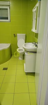 Bathroom with green tiles, bathtub, toilet, and washbasin. - image 9