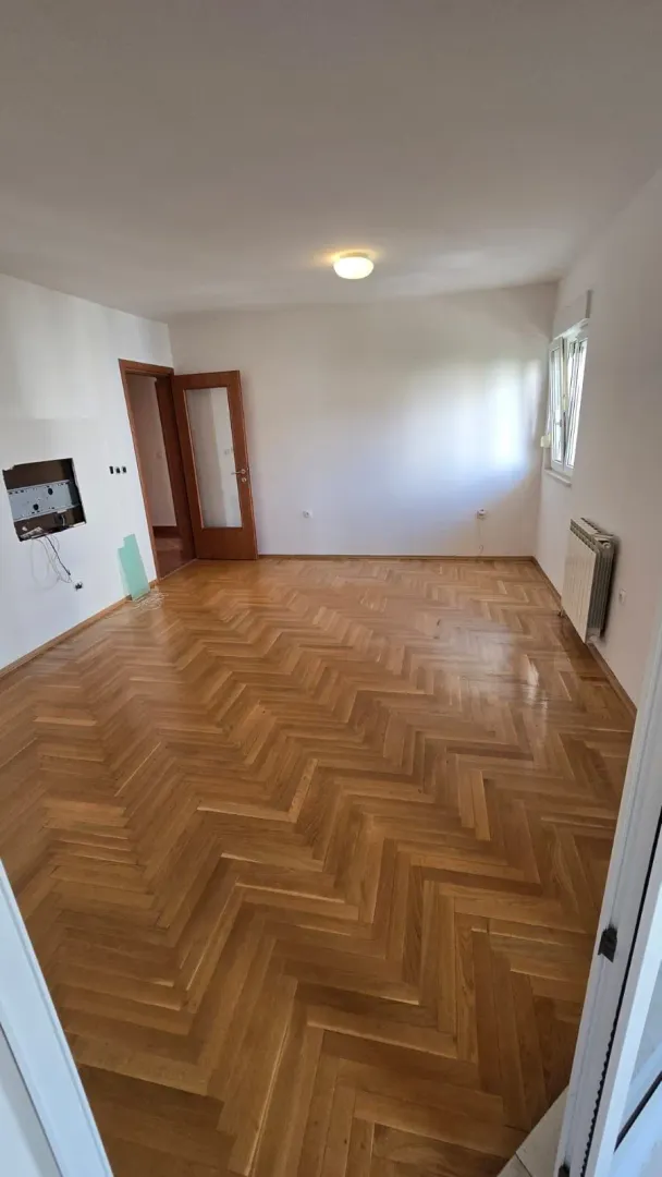 Prazna soba sa parketom i bijelim zidovima.