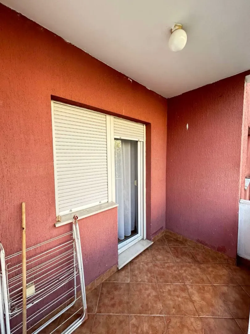 Natkriveni balkon sa popločanim podom i roletnama na prozorima.