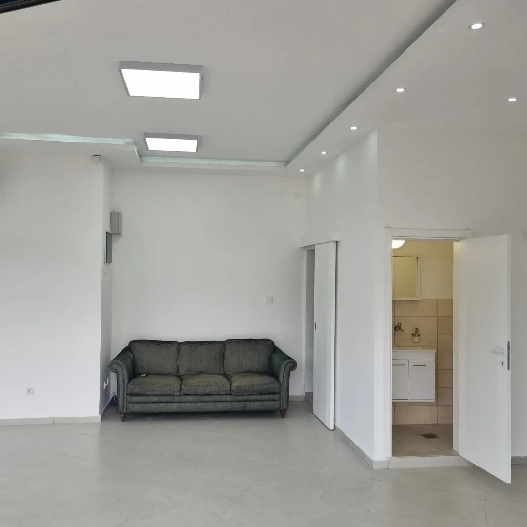 A bright room featuring a grey sofa and an open doorway leading to a bathroom.