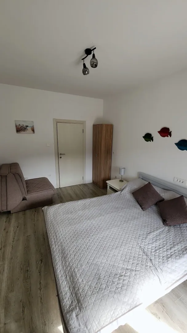 Namještena spavaća soba sa bračnim krevetom, foteljom i ormarom.