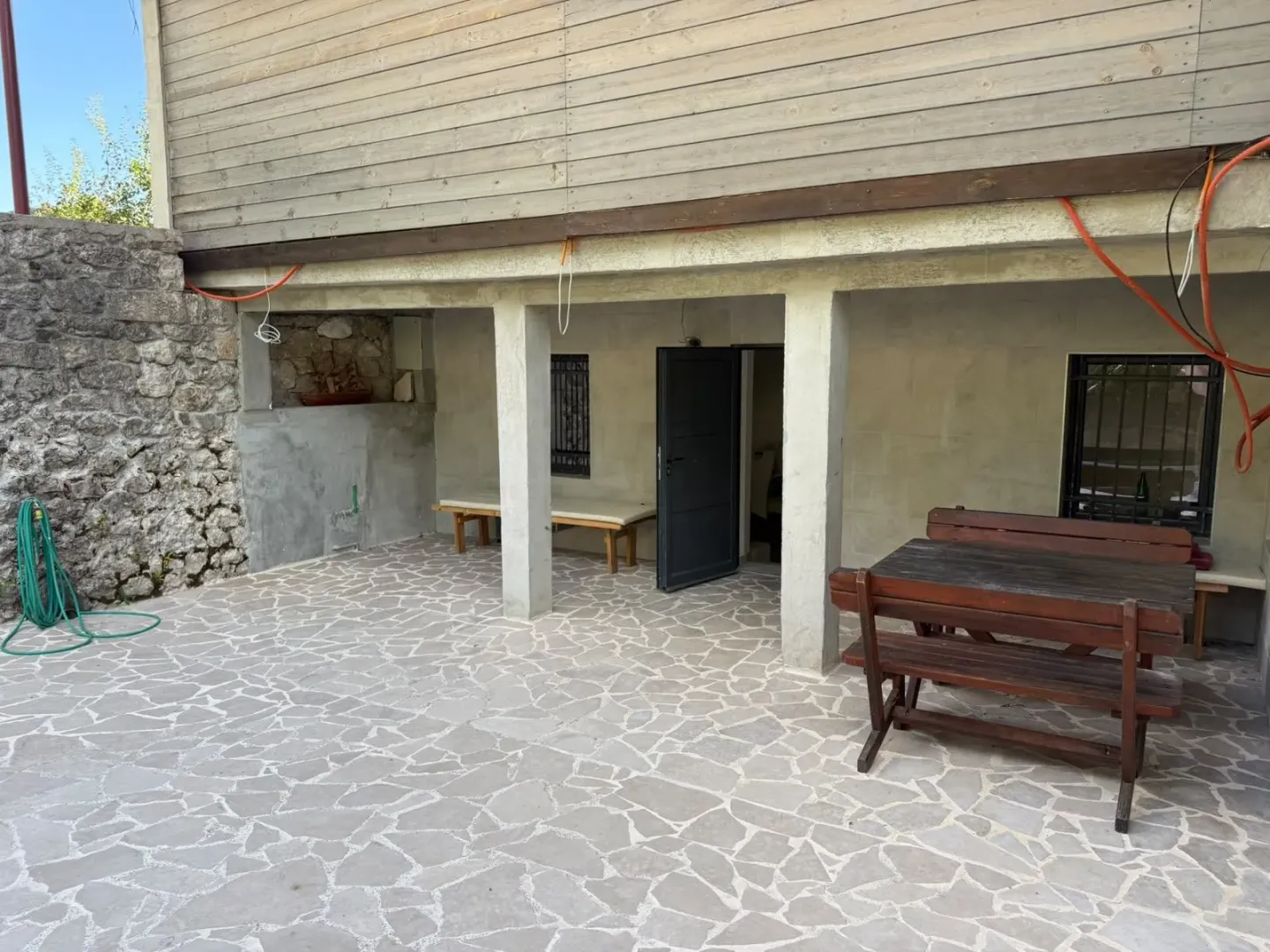 Dvorište sa popločanim platoom i drvenom garniturom u prizemlju kuće.