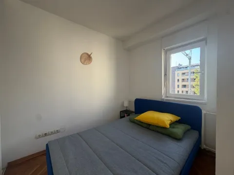 Manja spavaća soba sa krevetom i prozorom koji gleda na zgradu. - image 4