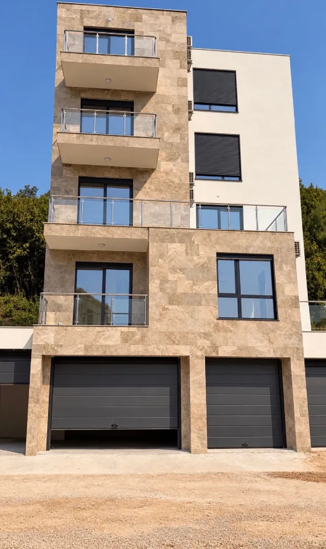 Pogled na spoljašnjost moderne stambene zgrade sa balkonom i garažom.
