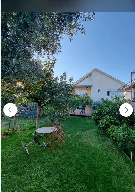 Dvorište sa zelenim travnjakom, drvećem i kućom u pozadini.