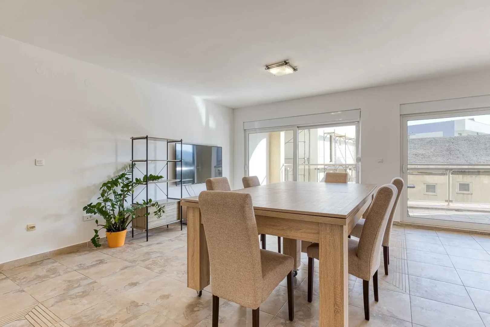 Living room with a dining table and chairs, wall-mounted TV, and access to the terrace.