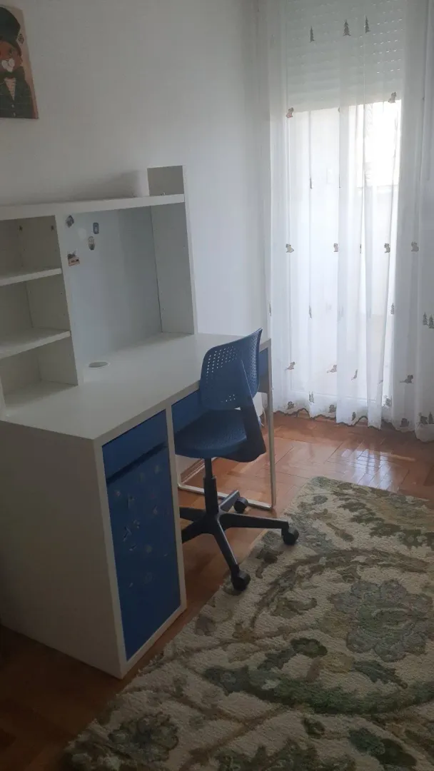A study corner with a white desk and a blue chair next to the window.