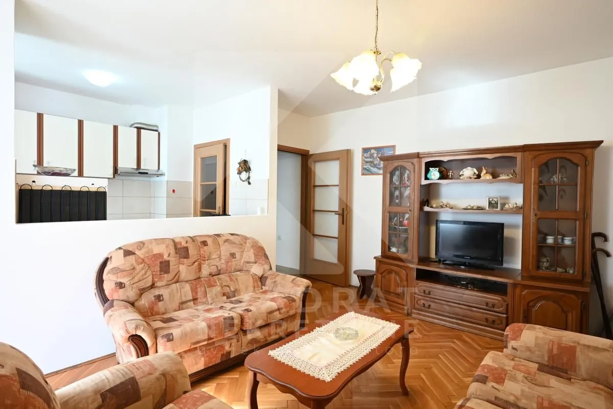 Living room with sofa set, TV unit, and a view of the kitchen in the background.