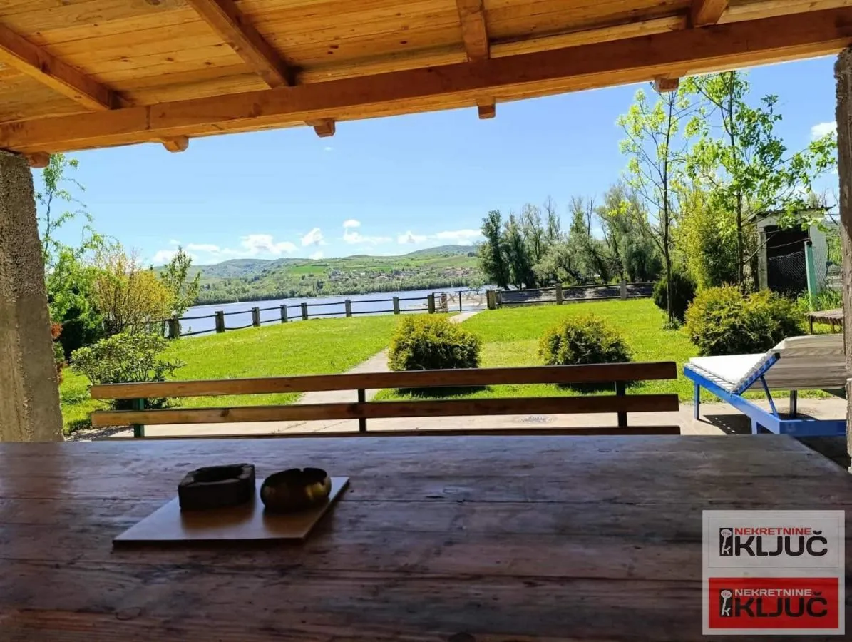 Covered terrace with a wooden table and a view of the yard and nature.