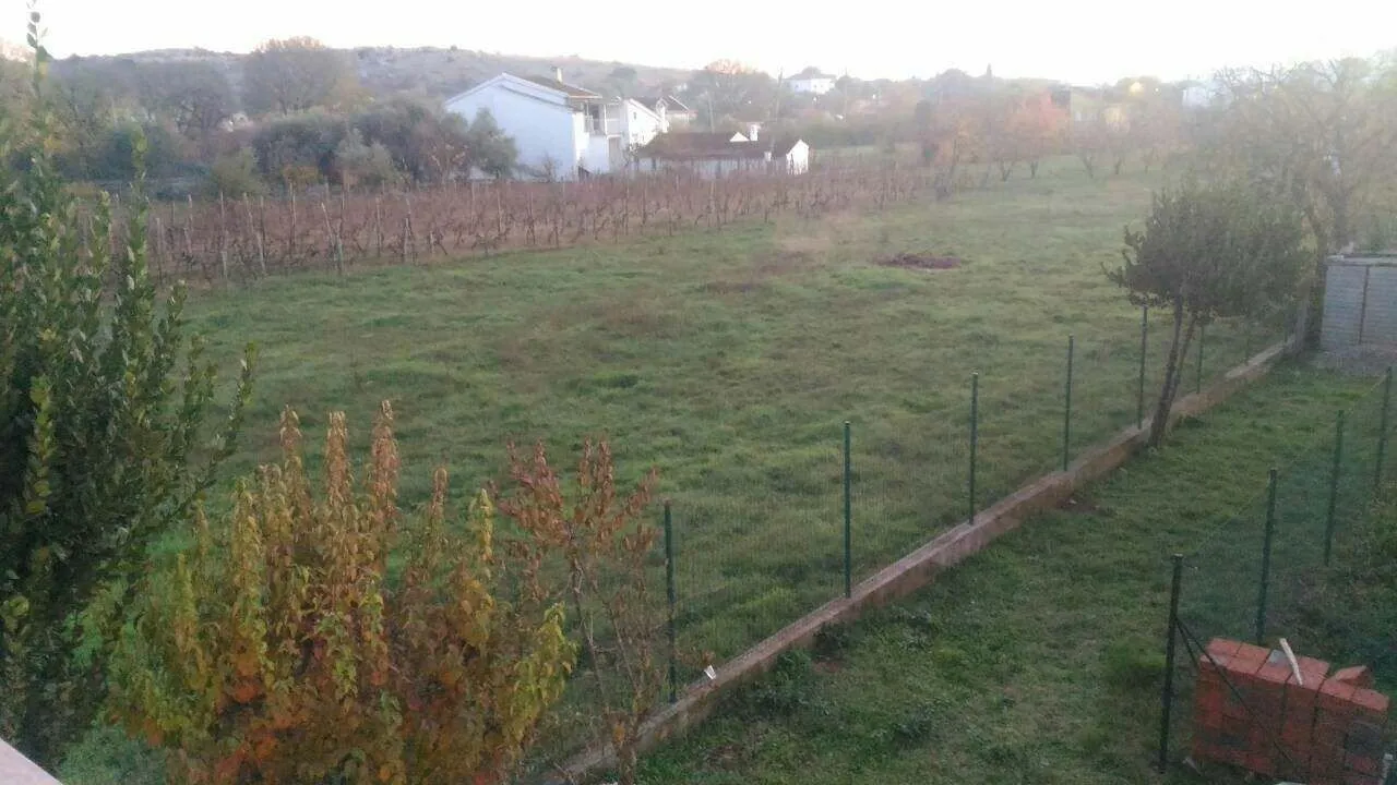 A fenced grassy plot with a view of surrounding houses and trees.