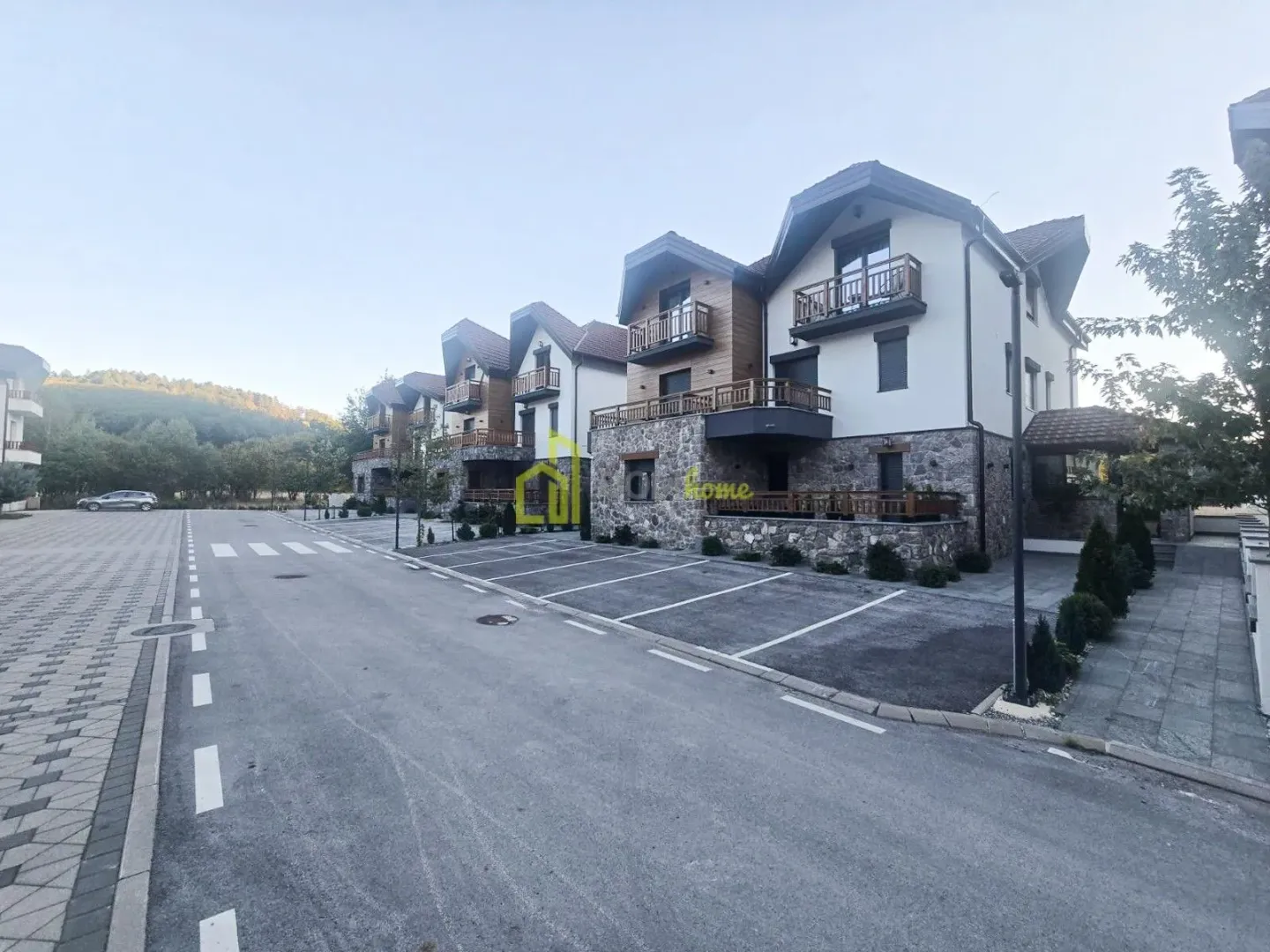 Pogled na spoljašnjost zgrade sa parkingom i uređenim dvorištem.