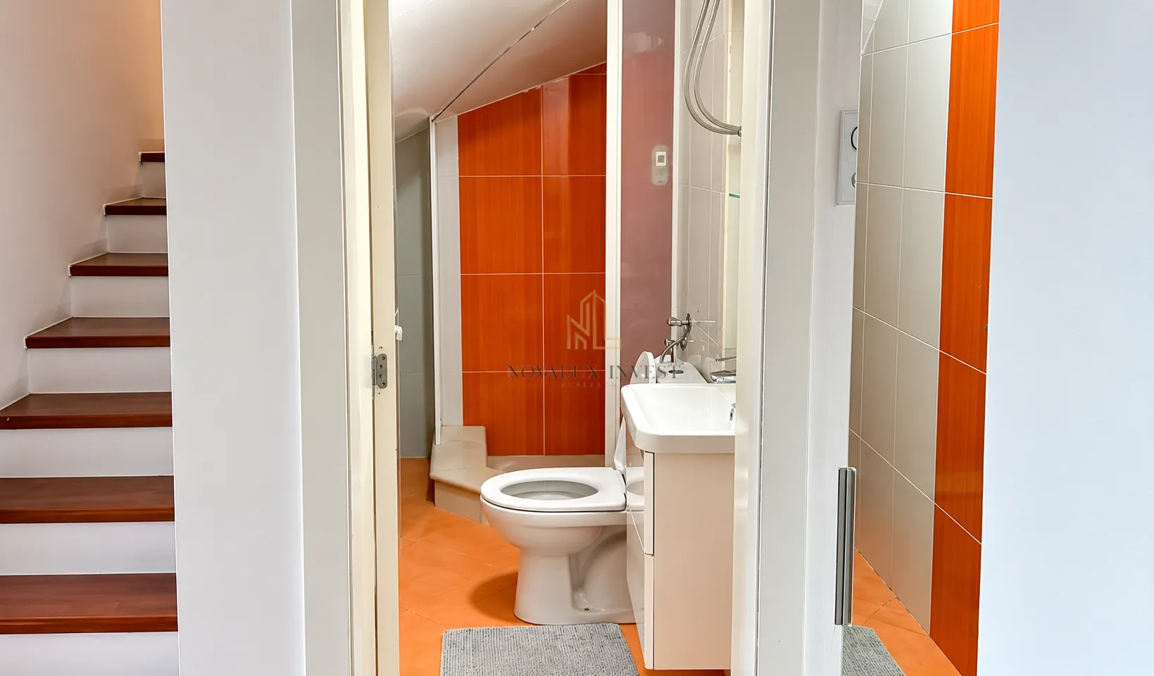 View of the bathroom with orange tiles and stairs on the left.