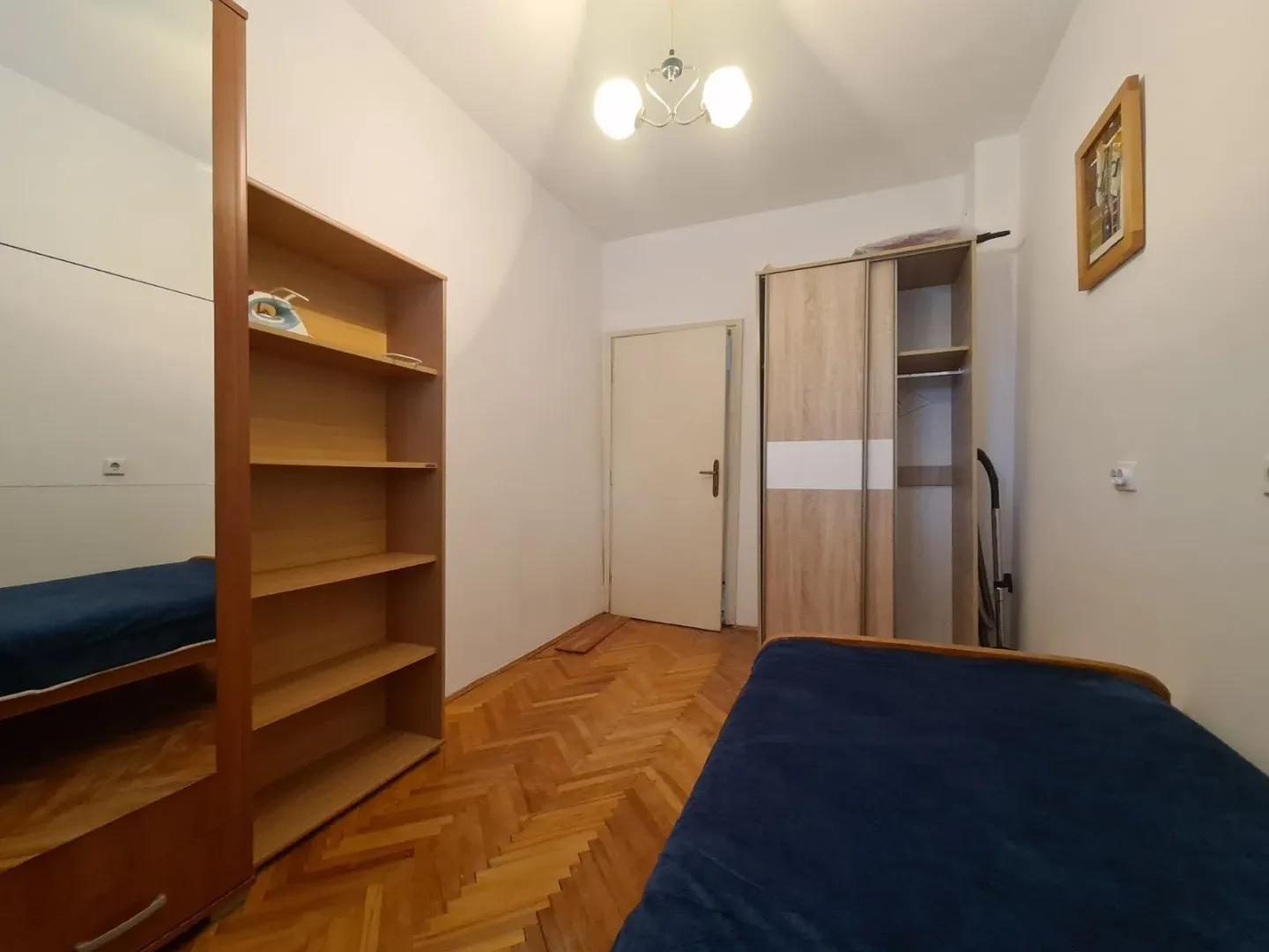A simply furnished bedroom with wooden parquet flooring and wardrobes.