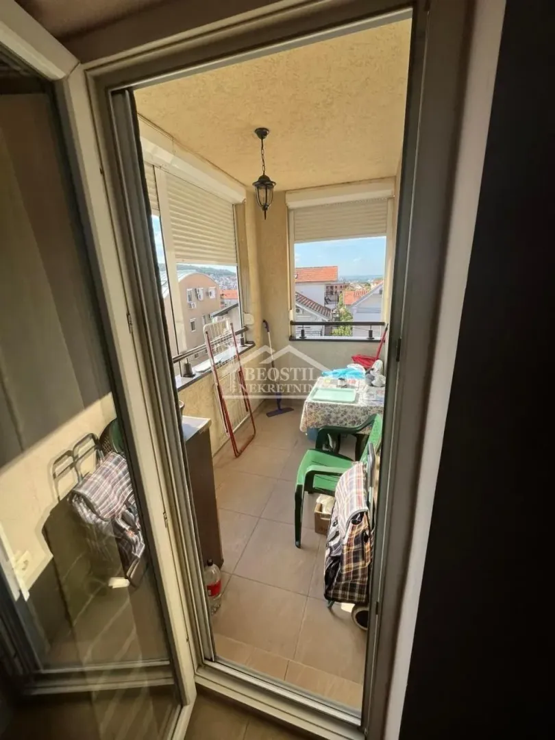Zastakljeni balkon sa pogledom na naselje i krovove okolnih zgrada.