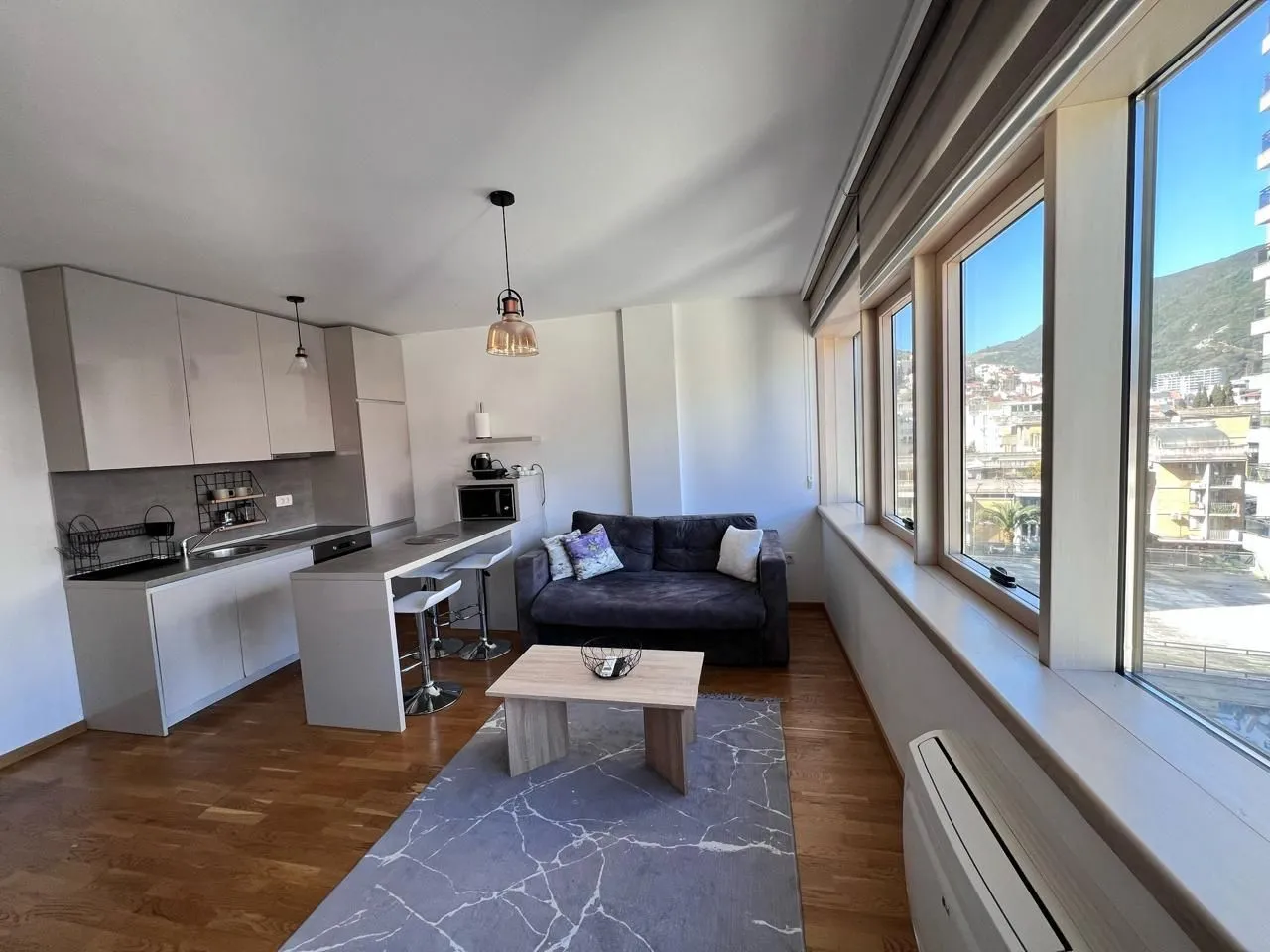 Living room with kitchen and dining bar, featuring views through large windows.