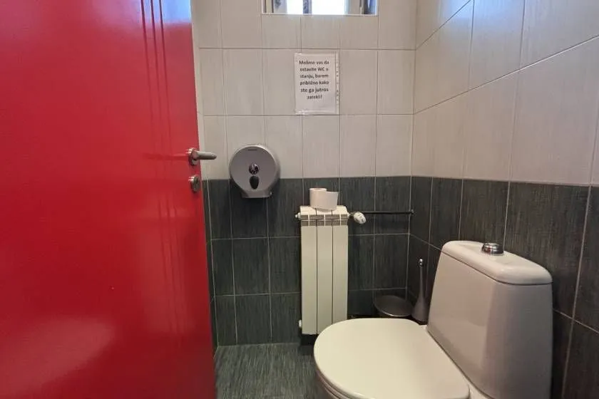 Smaller bathroom with a toilet, radiator and a red door.