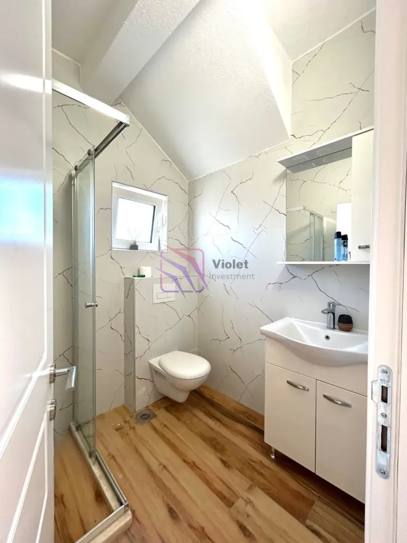 Manje kupatilo sa tuš kabinom, umivaonikom i ugradnom wc šoljom.