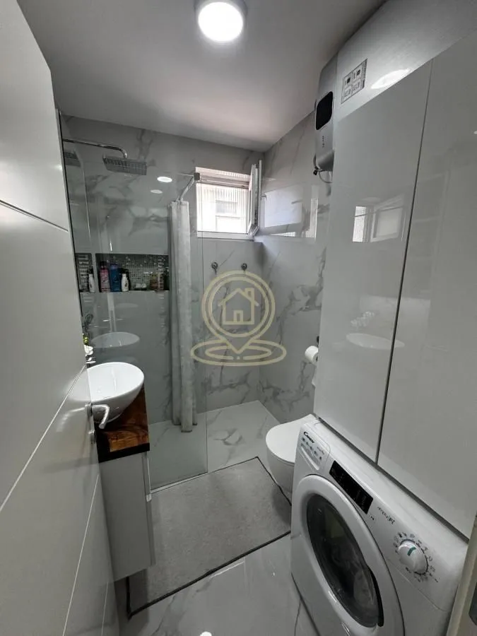 Moderno kupatilo sa tuš kabinom, umivaonikom i veš mašinom.