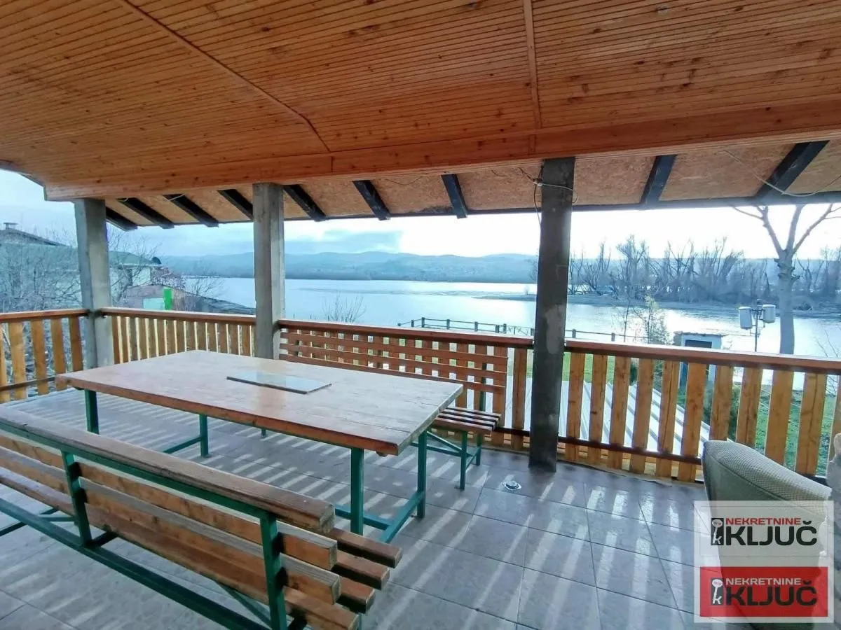 Covered terrace with a wooden table and benches and a river view.