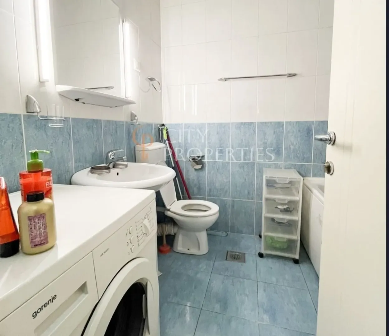 Bathroom with blue tiles, a washing machine, and white sanitaryware.
