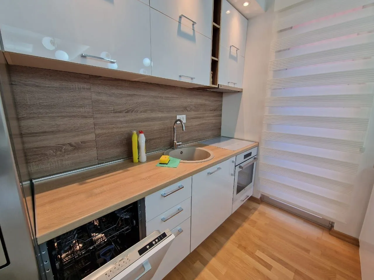 Modern white kitchen with wooden elements and built-in appliances.