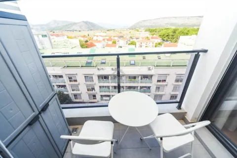 Manji namješteni balkon sa stolom, dvije stolice i pogledom na okolne zgrade i brda. - image 2