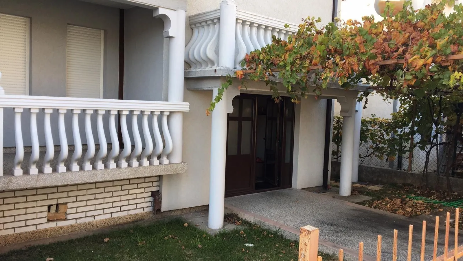 Entrance to the house with white pillars, a balustrade, and a grapevine.